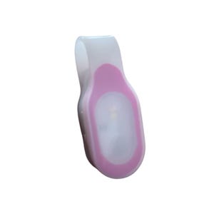 May include: A white and pink LED safety light with a clip. The light has a pink border around the oval-shaped light. The clip is white and curved. The light is designed to be clipped onto clothing or accessories.