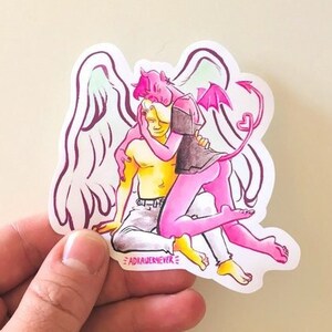 May include: A sticker featuring a pink and yellow illustration of an angel and a devil embracing. The angel has wings and the devil has a tail with a heart at the end. The text "#ADIAUENEVER" is at the bottom of the sticker.