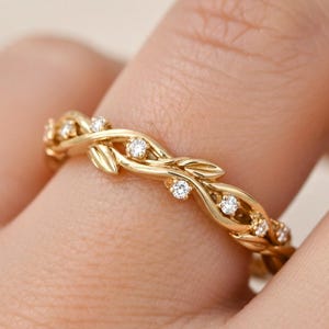 May include: A gold ring featuring a delicate, intertwined vine design. The band is crafted with polished gold metal shaped into organic leaf motifs, accented with small, round, clear, sparkling gemstones set along the vine pattern.