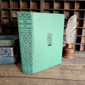May include: A vintage copy of "The Decameron of Boccaccio, Illustrated" with a light green cover. The spine has black scrollwork and "Blue Ribbon Classics." A feather quill and inkwell are also visible.