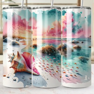 May include: A set of three white stainless steel tumblers with a watercolor design of a beach scene. The design features a large seashell, ocean, and colorful sky in shades of pink, blue, and orange. The tumblers have a straw.