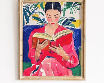 May include: A framed art print depicting a person with dark hair wearing a bright pink top, sitting on a blue sofa while reading an open book with a red cover. The background features green foliage and yellow accents in a painterly style.