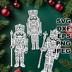 May include: Three white, ornate nutcracker ornaments with intricate cut-out designs. The ornaments are in different poses and sizes, with one holding a staff. The background is a dark green with Christmas decorations and the text "SVG, DXF, EPS, PNG, JPEG".