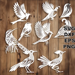 May include: A set of ten white paper cut-out bird silhouettes. The birds are arranged in a variety of poses, including flying, perched, and standing. The birds are all facing the viewer. The background is a wooden surface.