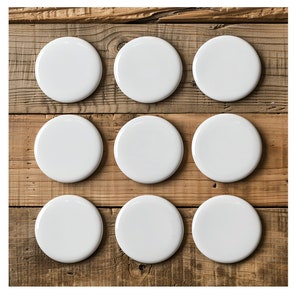 May include: Nine blank, white, round coasters arranged in a grid pattern. The coasters are made of a glossy material and are set on a rustic, weathered wooden surface. The coasters are ready for customization.