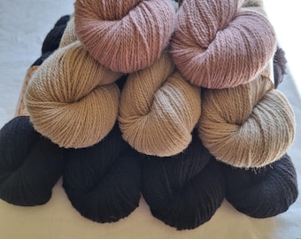 Könnte beinhalten: Eine Sammlung von Garnknäueln in verschiedenen neutralen Farben, darunter Schwarz, Beige und Mauve. Das Garn ist eng gewickelt und zeigt die Textur der Fasern. Die Knäuel sind zusammen angeordnet, was auf ein Bastel- oder Strickprojekt hindeutet.