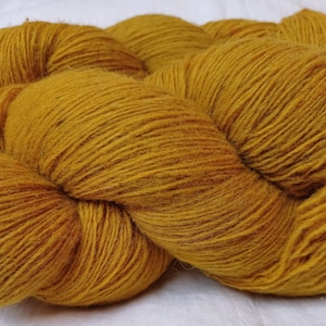 Può includere: Un gomitolo di filato giallo dorato, realizzato con fibre morbide e soffici. Il filato è avvolto strettamente e ha una texture liscia e uniforme.