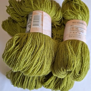 Peut inclure: Plusieurs écheveaux de fil vert olive sont présentés. Chaque écheveau est enveloppé d'une étiquette en papier avec du texte et un code-barres. Le fil semble être de la laine, avec une longueur de 350 mètres par écheveau.