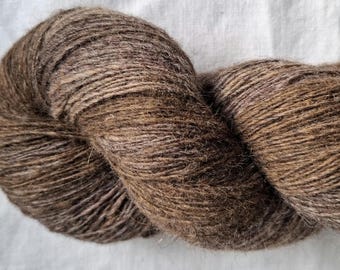 May include: A twisted skein of yarn in a variegated medium brown color. The fiber has a visible, slightly fuzzy texture with subtle tonal variations ranging from light tan to dark chocolate brown throughout the tightly wound strands.