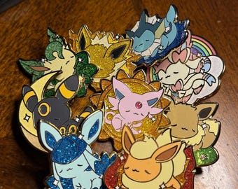 Puede incluir: Una colección de nueve pines de esmalte con diferentes personajes de Pokémon. Los pines son todos de color dorado y tienen un acabado brillante. Cada pin presenta un personaje de Pokémon diferente en una pose para dormir. Los personajes incluyen Eevee, Flareon, Vaporeon, Jolteon, Espeon, Umbreon, Glaceon, Leafeon y Sylveon.
