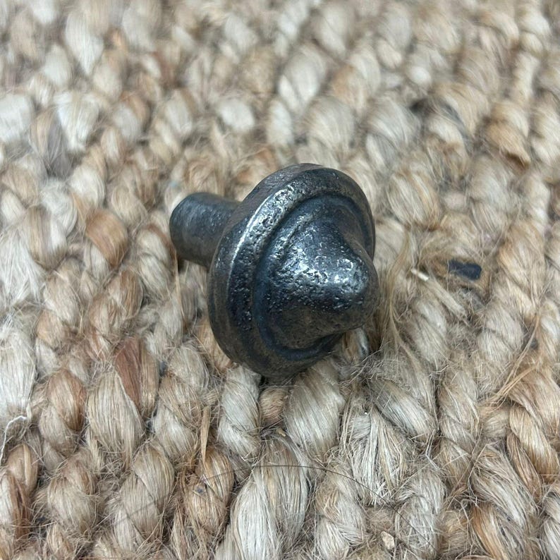 May include: A black metal cabinet knob with a pointed top and a circular base. The knob has a distressed finish.