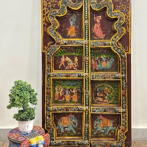 May include: A pair of intricately carved wooden doors with colourful painted scenes of people and elephants. The doors are decorated with floral motifs and have a dark brown finish.