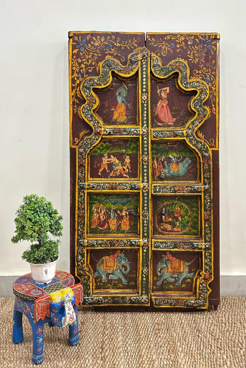 May include: A pair of intricately carved wooden doors with colourful painted scenes of people and elephants. The doors are decorated with floral motifs and have a dark brown finish.