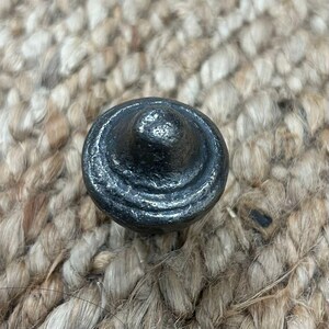 Pode incluir: Uma maçaneta de armário de metal preto com a parte superior arredondada e um design circular elevado.