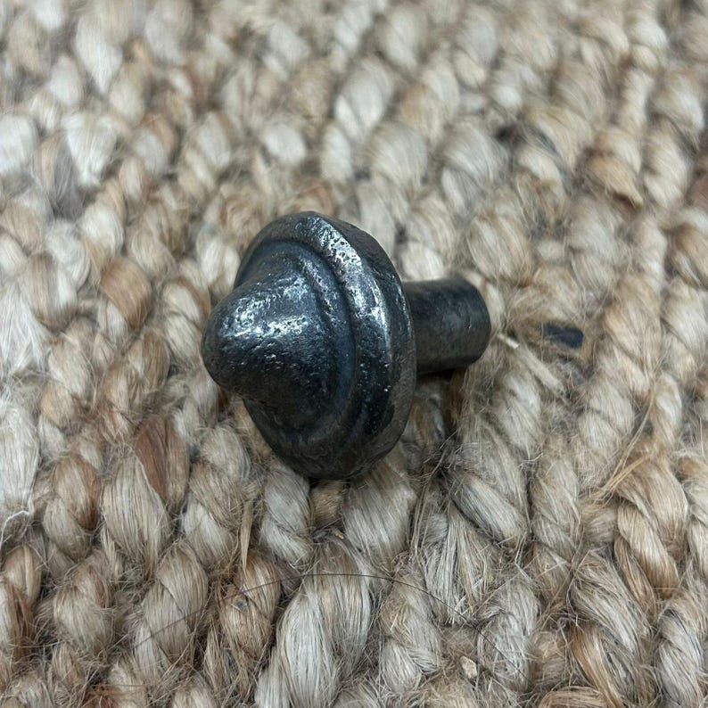 May include: A black metal cabinet knob with a rounded, domed top and a single screw hole. The knob has a slightly textured surface.