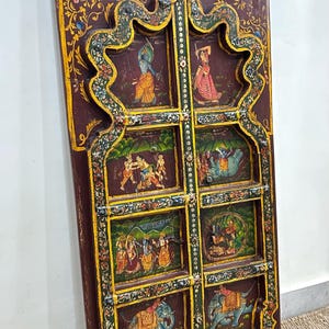 May include: A pair of intricately carved wooden doors with a dark brown background and colourful painted scenes of people and elephants. The doors are decorated with gold and green accents.