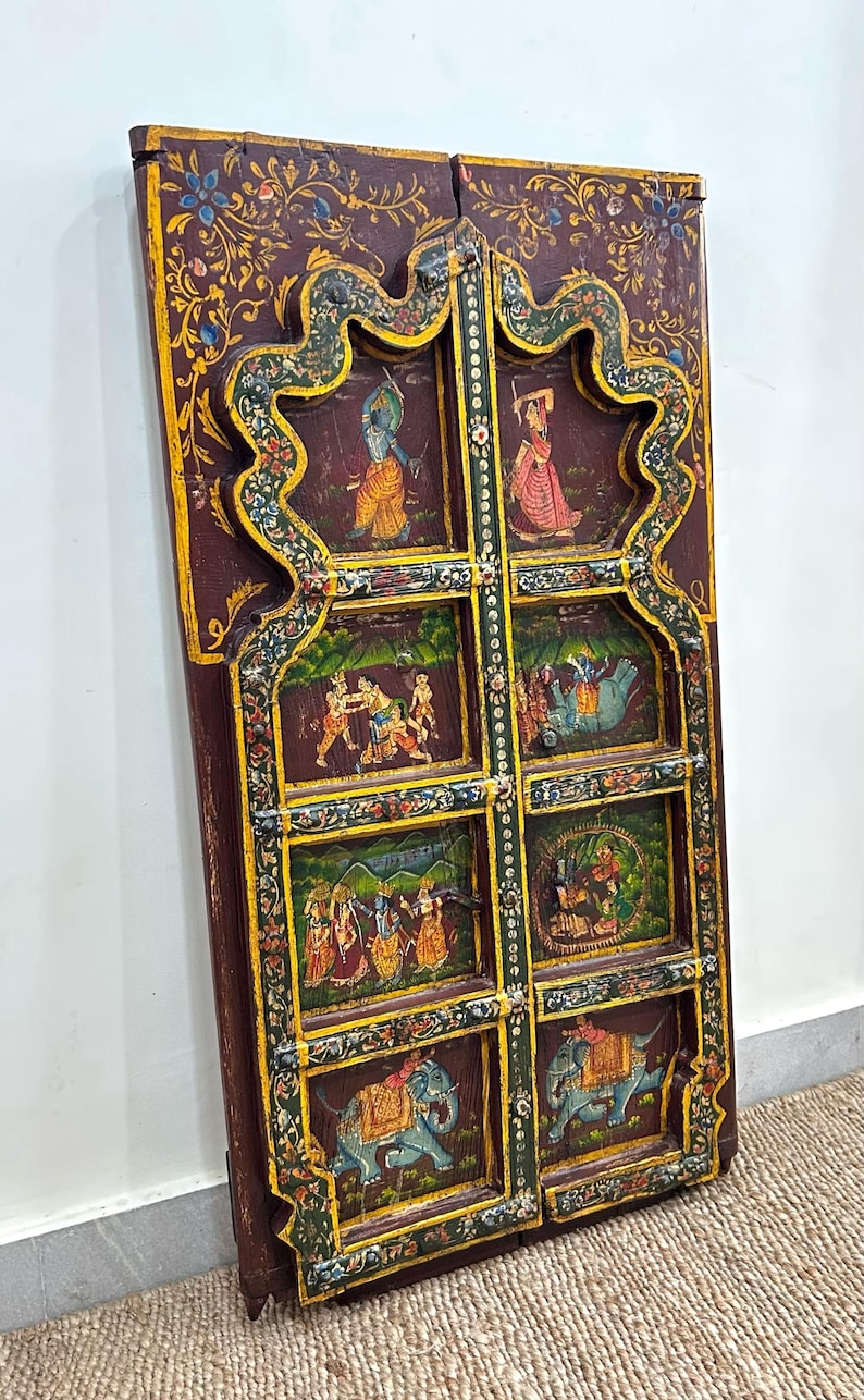 May include: A pair of intricately carved wooden doors with a dark brown background and colourful painted scenes of people and elephants. The doors are decorated with gold and green accents.