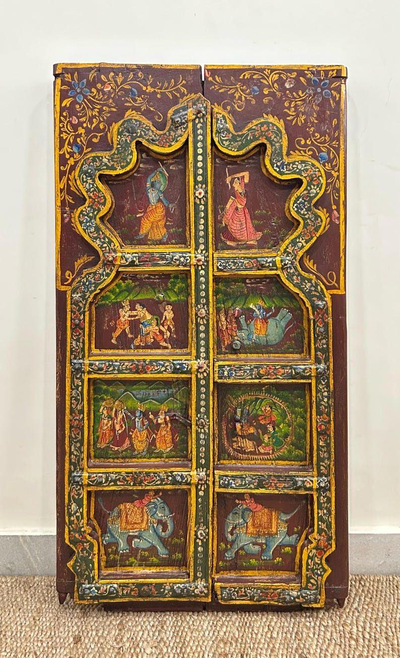 May include: A pair of wooden doors with intricate carvings and colourful paintings depicting scenes from Hindu mythology. The doors are painted in shades of red, green, blue, and gold.