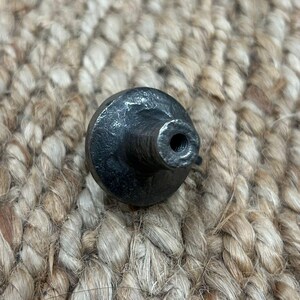May include: A black metal knob with a round base and a threaded hole in the centre. The knob has a rough, textured surface.
