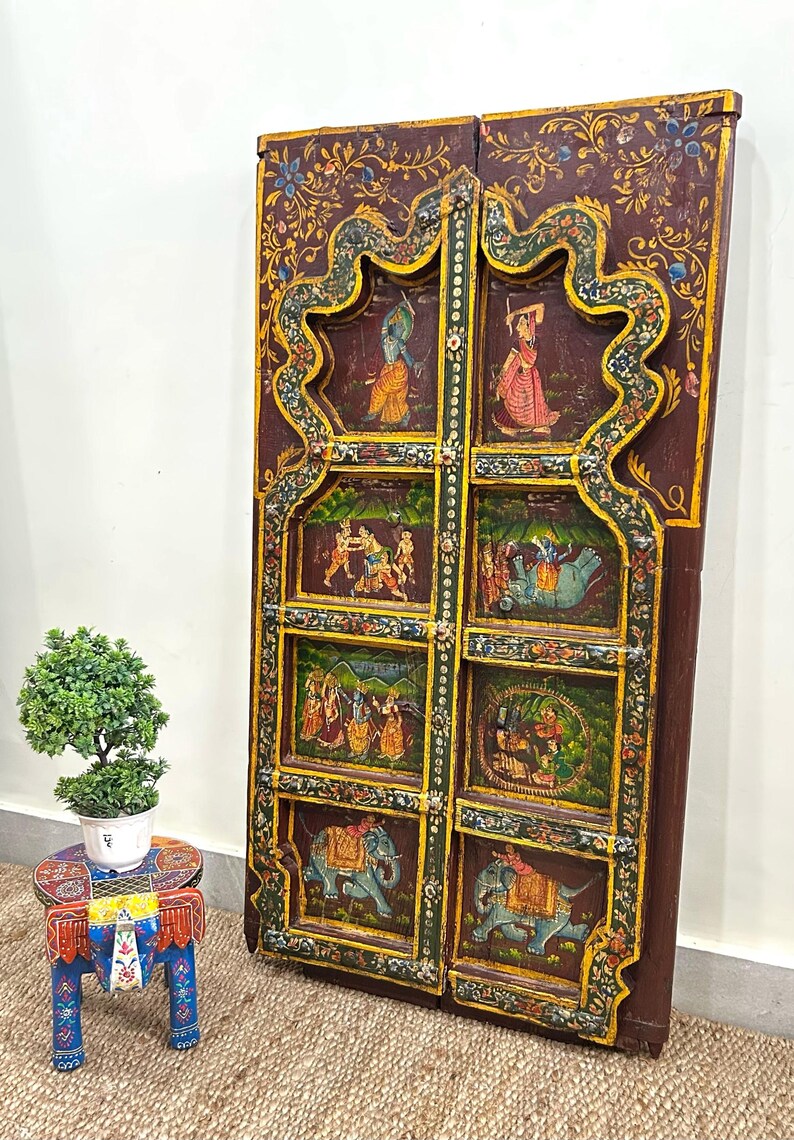 May include: A pair of intricately carved wooden doors featuring colourful painted scenes of people and elephants. The doors are decorated with floral patterns and have a dark brown finish.
