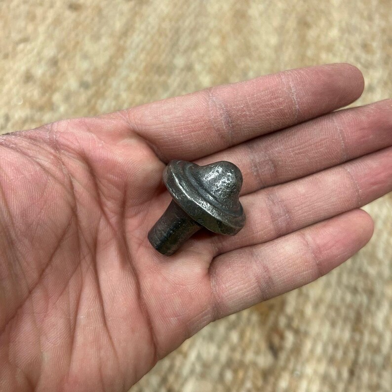 May include: A small, silver-coloured metal knob with a rounded top and a circular base. The knob has a slightly textured surface.