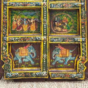 May include: A wooden door with intricate carvings and colourful painted scenes. The door is divided into four panels, each featuring a different scene. The top panels depict figures in traditional Indian clothing, while the bottom panels feature elephants with riders. The door is painted in shades of yellow, green, blue, and red.