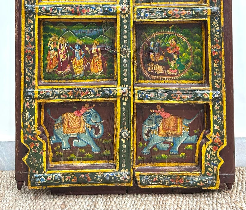 May include: A wooden door with intricate carvings and colourful painted scenes. The door is divided into four panels, each featuring a different scene. The top panels depict figures in traditional Indian clothing, while the bottom panels feature elephants with riders. The door is painted in shades of yellow, green, blue, and red.
