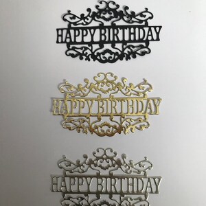 May include: Three decorative "Happy Birthday" signs with intricate scrollwork designs. The top sign is black, the middle sign is gold, and the bottom sign is silver.