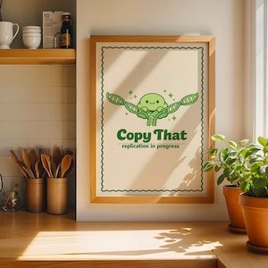 May include: A framed wall art print featuring a light cream background with a green scalloped border. The central graphic shows a smiling green character holding a DNA strand with the text Copy That and replication in progress below it.