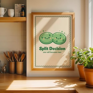 May include: A framed wall art print featuring a light cream background with a scalloped border. The graphic shows two connected green cells with smiling faces and sparkles. The text reads Split Decision and one cell becomes two.