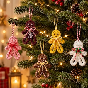 May include: Five crocheted gingerbread person ornaments hanging on a Christmas tree. The figures are pink, dark red, yellow, brown, and white, each featuring a small bow, bead eyes, and a hanging string. The red one has a snowflake detail.