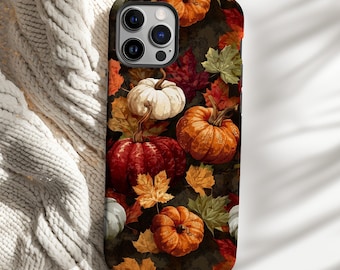 May include: A phone case featuring a fall-themed design with pumpkins and leaves. The case showcases a dark background with orange, red, and white pumpkins, along with autumn leaves in shades of yellow, green, and red. The case is designed to fit a smartphone.