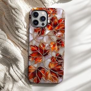 May include: A smartphone case featuring a stained-glass design of autumn maple leaves in shades of red, orange, and brown. The leaves are outlined in gold against a pearlescent background. The case has a glossy finish.