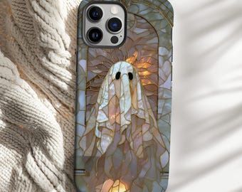 May include: A phone case featuring a stained-glass design of a ghost. The ghost is white with black eyes and is set against a backdrop of warm, golden light. The case has a dark blue border and a glossy finish.