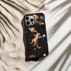 May include: A black phone case with a space-themed design featuring a cat floating in space with planets and stars. The case has a camera cutout and a black background.