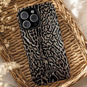 May include: A phone case with a leopard print design in shades of brown, black, and cream. The case has a camera cutout and the name "Helena" in a script font. The case is resting on a woven wicker tray.