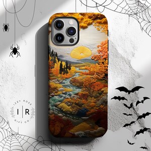 May include: A phone case featuring a landscape design with a river, trees, and a yellow sun. The case has a colorful autumn scene with shades of orange, yellow, and green. The brand name "Izzy Rose Gift Co." is printed on the case.