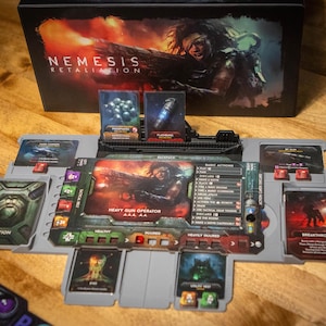 Pode incluir: Jogo de tabuleiro "Nemesis: Retaliation" com caixa e componentes. O tabuleiro é cinza com vários cartões e fichas. A caixa apresenta uma ilustração de guerreiro. Os cartões exibem detalhes de ação e informações de personagens.