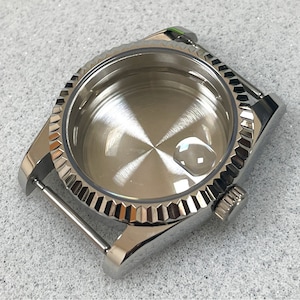 Puede incluir: Una caja de reloj plateada brillante con un bisel estriado y una corona. La caja del reloj tiene un interior pulido y una lengüeta para la correa del reloj. La caja del reloj está hecha de acero inoxidable.