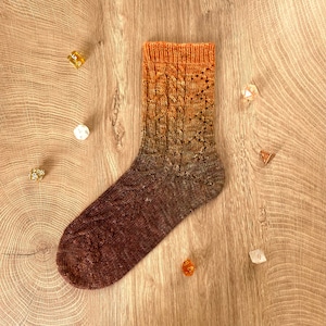 May include: A pair of knitted socks with a cable pattern and a gradient of orange and brown colors.