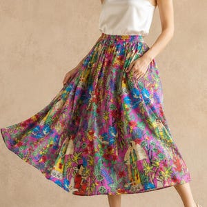 May include: A woman wearing a white camisole top and a colorful floral print midi skirt. The skirt features a vibrant mix of pink, blue, green, and yellow hues. The model is also wearing high-heeled sandals.