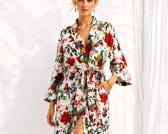 May include: A long-sleeved, calf-length robe featuring a vibrant floral and bird pattern in shades of red, green, and yellow on a white background. The garment includes a V-neckline, a matching fabric waist tie, and a front slit opening.