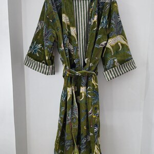 May include: A green velvet robe with a cheetah print and tropical leaf pattern. The robe has a white and green striped lining and a matching tie belt.