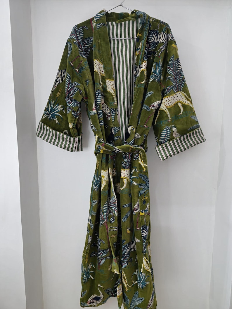 May include: A green velvet robe with a cheetah print and tropical leaf pattern. The robe has a white and green striped lining and a matching tie belt.