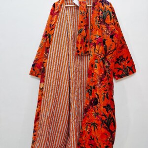 May include: An orange floral print robe with a striped interior. The robe is hanging on a wooden hanger. The floral pattern includes red, green, and black accents.