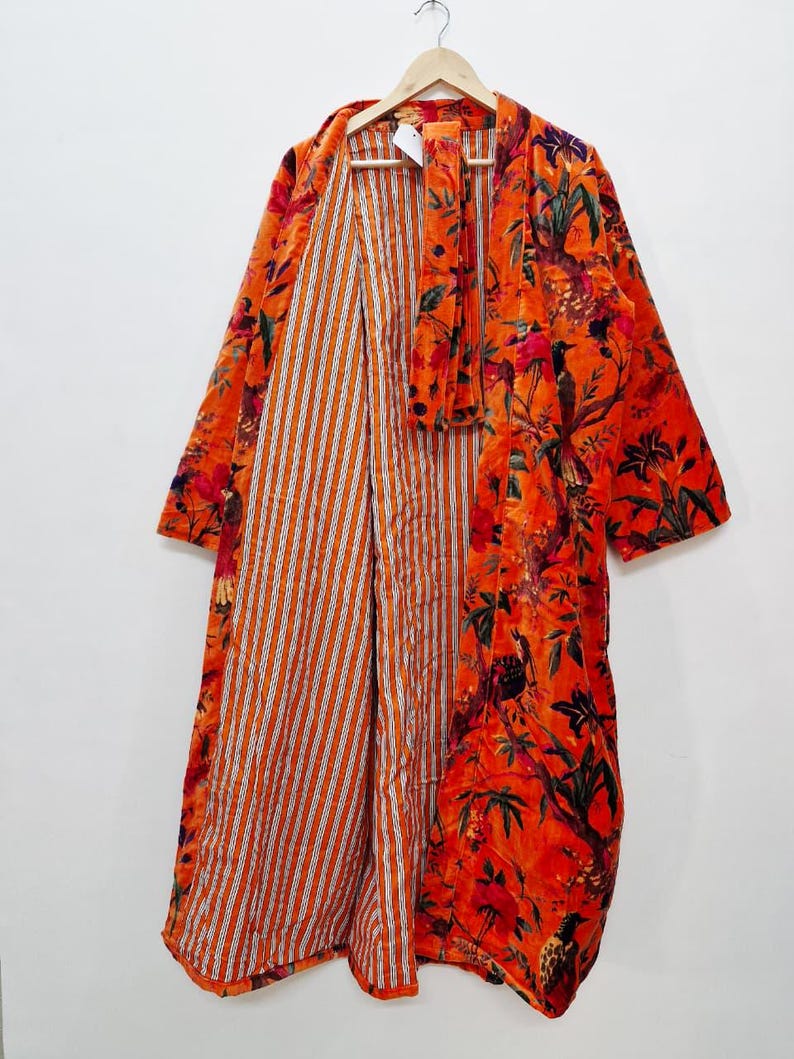 May include: An orange floral print robe with a striped interior. The robe is hanging on a wooden hanger. The floral pattern includes red, green, and black accents.