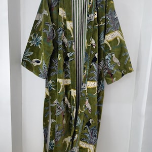 May include: A green velvet robe with a jungle print featuring zebras, leopards, toucans, and palm trees. The robe has a white and green striped lining.