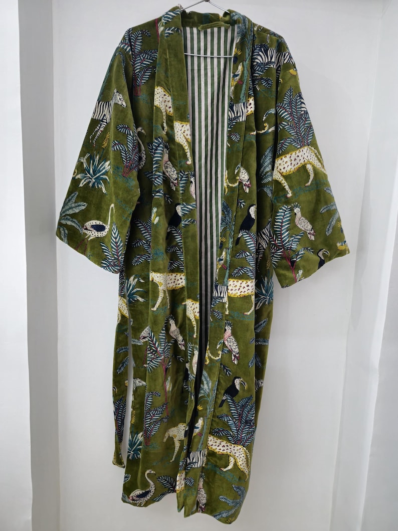 May include: A green velvet robe with a jungle print featuring zebras, leopards, toucans, and palm trees. The robe has a white and green striped lining.