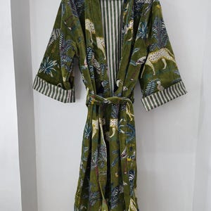 May include: Green velvet robe with a jungle animal print, including leopards and zebras. The robe has a striped interior and cuffs, and a matching belt. The robe is hanging on a hanger.