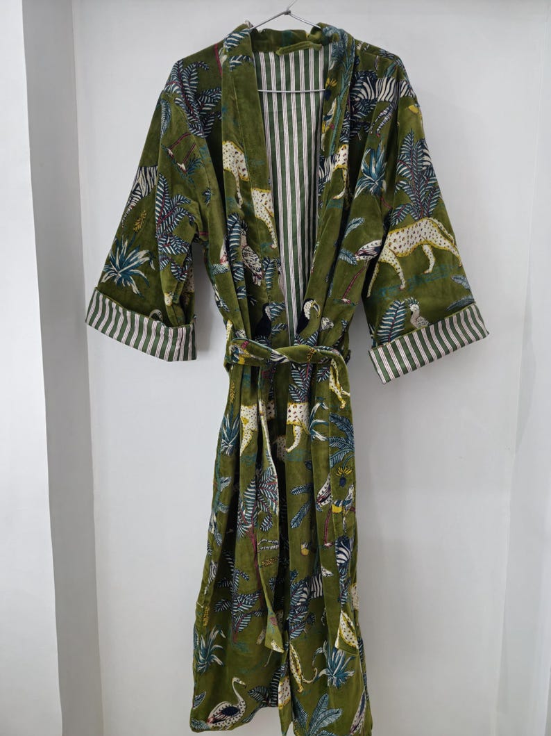 May include: Green velvet robe with a jungle animal print, including leopards and zebras. The robe has a striped interior and cuffs, and a matching belt. The robe is hanging on a hanger.